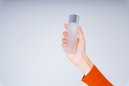 Hand of young woman holding bottle of perfume or lotion on white background.の写真素材