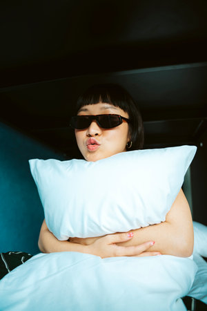 Portrait of cheerful asian short hair woman wearing sunglasses on white bed.の写真素材