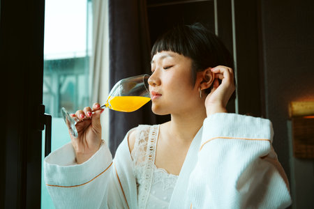 Asian short hair woman in white bathrobe enjoy breakfast with orange juice in hotel room.の写真素材