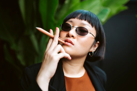 Cool asian short hair woman wearing sunglasses holding pen like cigarette.の写真素材