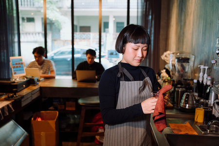 Asian short hair woman barista cleaning glass cup behind the bar in cafe.の写真素材