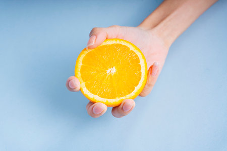 Hand of woman holding a slice of orange on blue background.の写真素材