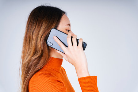 Side view - Asian woman in orange sweater talking on the phone isolate on white background.の写真素材