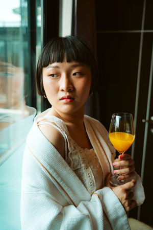 Asian short hair woman in white bathrobe enjoy breakfast with orange juice in hotel room.の写真素材