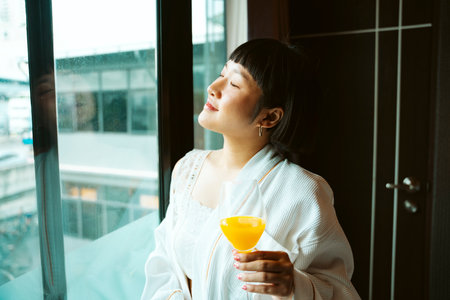 Asian short hair woman in white bathrobe enjoy breakfast with orange juice in hotel room.の写真素材