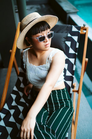 Young asian woman wearing sunglasses and hat laying on beach chair in hotel near swimming pool.の写真素材