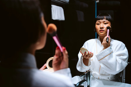 Short hair asian woman using powder brush stick infront of the mirror.の写真素材
