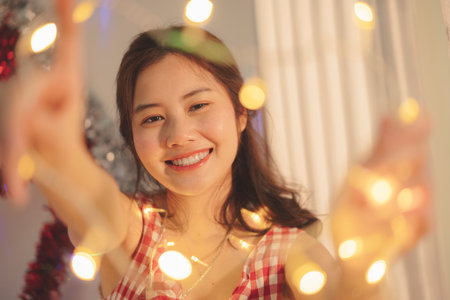 Close up - Beauty young asian woman black hair playing christmas light at home.の写真素材