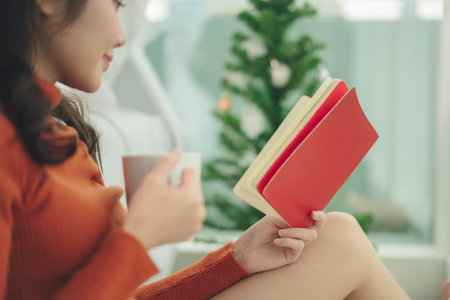 Side view - Woman wearing red sweater reading a book and holding hot coffee cup.の写真素材