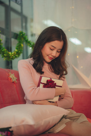 Young asian woman wearing sweater with gift box sitting on sofa in christmas event.の写真素材