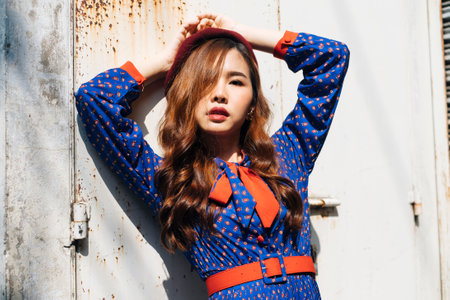 Medium shot of wavy brunette woman in blue and red retro dress standing like the supermodel at the old warehouse in sunlight.の写真素材