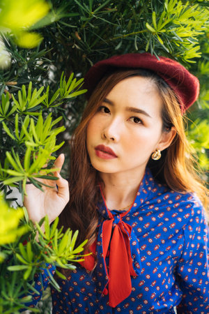 Portrait picture of wavy brunette woman in blue and red retro dress standing at the green leaf,...