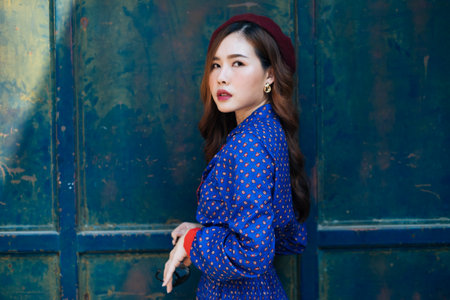 Portrait shot of wavy brunette woman in blue and red retro dress and red lip standing in front of rusty door of warehouse.の写真素材