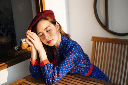 Wavy brunette woman in blue and red retro dress sitting at the wooden table next to glass window with owl.の写真素材