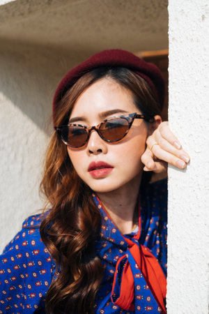 Wavy brunette woman in blue and red retro dress standing at the white frame of the building and prop her head on the frame, close up.の写真素材