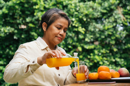 Senior elder woman pouring orange juice from glass bottle outdoors at park.の写真素材