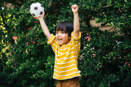 Cheerful asian boy holding football showing hands in the air at park.の写真素材