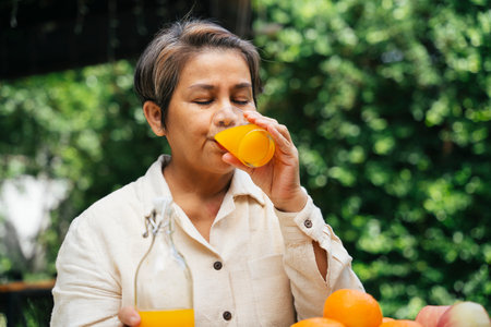 Senior elder woman drinking orange juice from glass cup outdoors at park.の写真素材