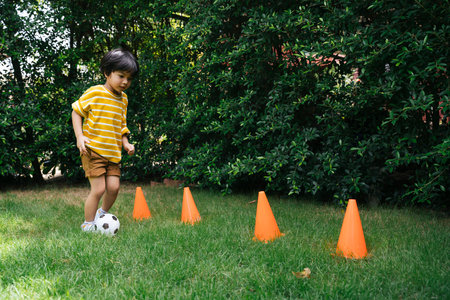Asian boy practice dribble football with cone on grass field.の写真素材