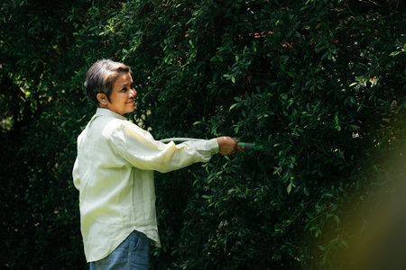 Senior elderly old woman watering plant with garden hose.
