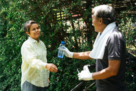 Grandmother giving bottle of water to grandfather mowing lawn at yard.