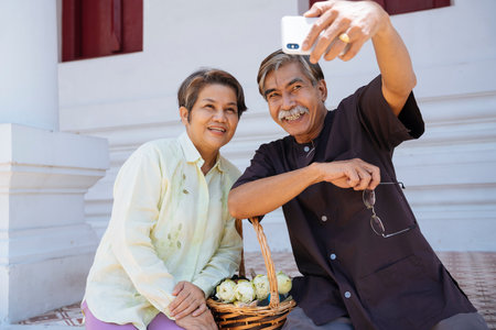 Asian senior elderly old couple taking selfie with smartphone in temple.