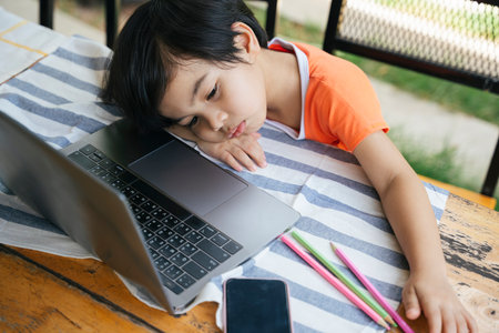 Top view - Bored asian kid tired of study from home infront of laptop.