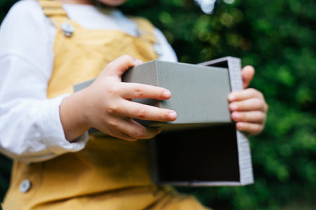 Kid opening grey birthday gift in a party outdoors at garden yard.の写真素材