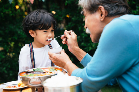 Grandfather feeding food to son in dinning party outdoor at yard.の写真素材
