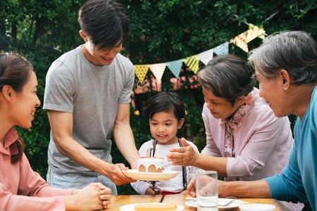 Asian family celebrate birthday party for a kid with cake outdoors.の写真素材