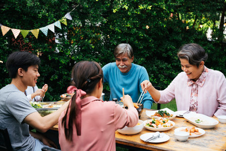 Asian family enjoy eating BBQ together at yard outdoors.の写真素材