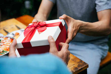 Son giving a gift box to father in party outdoors.の写真素材