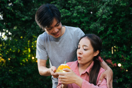 Asian man surprise girlfriend with birthday cake made of golden thread dessert. She blowing a candle.の写真素材