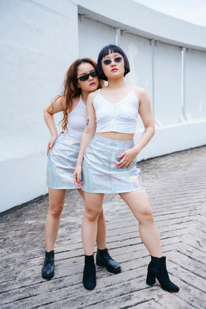 Fashion portrait of two young asian girls wear white vest and sunglasses on street.
