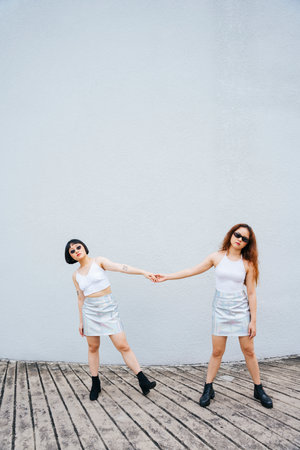 Portrait of two young asian women in white vest and sunglasses holding hand.の写真素材
