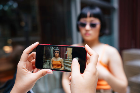 Asian young women wear sunglasses being taken picture with smartphone by her friend in cafe.
