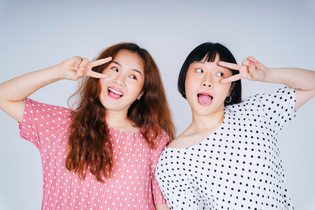 Portrait of two young asian women wearing pink and white palkadot isolate on white background.の写真素材