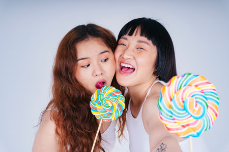 Close up portrait of two young asian women with rainbow sweet lollipop isolate on white.の写真素材