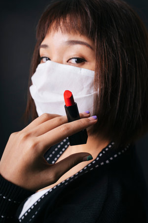 Beautiful asian thai woman short hair apply red lipstick on surgical mask isolate over black background. Beautiful on mask.の写真素材