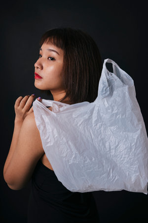 Beautiful asian thai woman short hair with plastic bag isolate over black background. Close up portrait. Plastic fashion.の写真素材