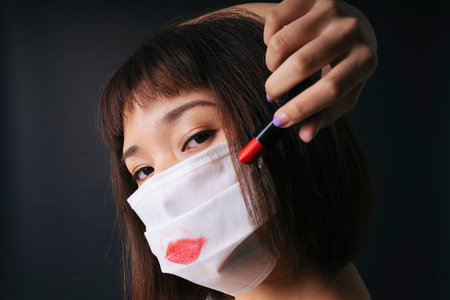 Beautiful asian thai woman short hair apply red lipstick on surgical mask isolate over black background. Beautiful on mask.の写真素材