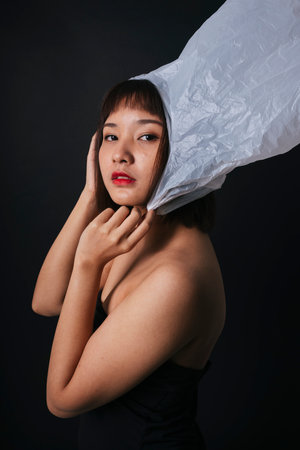 Beautiful asian thai woman short hair with plastic bag isolate over black background. Close up portrait. Plastic fashion.の写真素材