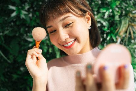 Close up asian thai woman apply cosmetic brush over green nature background outdoors.の写真素材