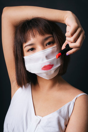 Beautiful asian thai woman short hair apply red lipstick on surgical mask isolate over black background. Beautiful on mask.の写真素材