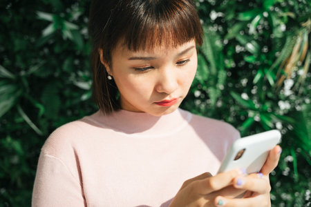 Beautiful asian thai woman in pink shirt using smartphone over green nature background.の写真素材
