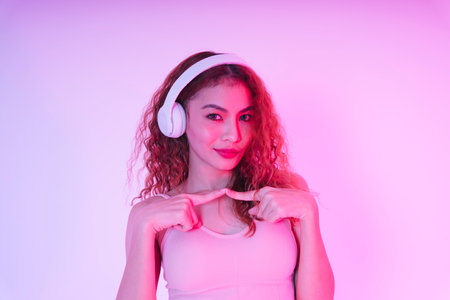 Portrait of young asian curly hair girl listen to music with headphone isolate on neon light background.の写真素材