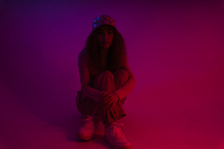Young asian woman wear hat and sweater sitting on the floor in neon light background.の写真素材