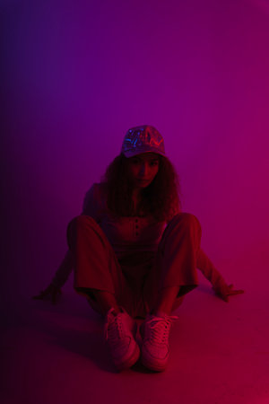 Young asian woman wear hat and sweater sitting on the floor in neon light background.の写真素材