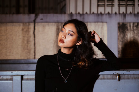 Fashionista girl in black sweater and jeans leaning against the truck in the light, medium close up.