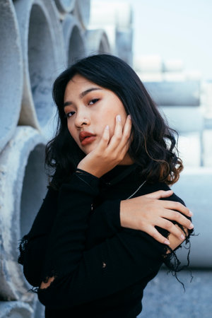 Medium shot of fashionista girl in black sweater and jeans standing next to the big concrete tube with crossed arms.の写真素材